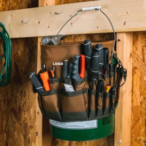 Brown 600D polyester heavy duty 5 gallon bucket tool bag caddy hanging on workshop wall, multi‑pocket hardware tool organizer for carpenter