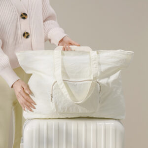 Cream white foldable nylon travel tote bag on suitcase, lightweight expandable carry-on duffel for women